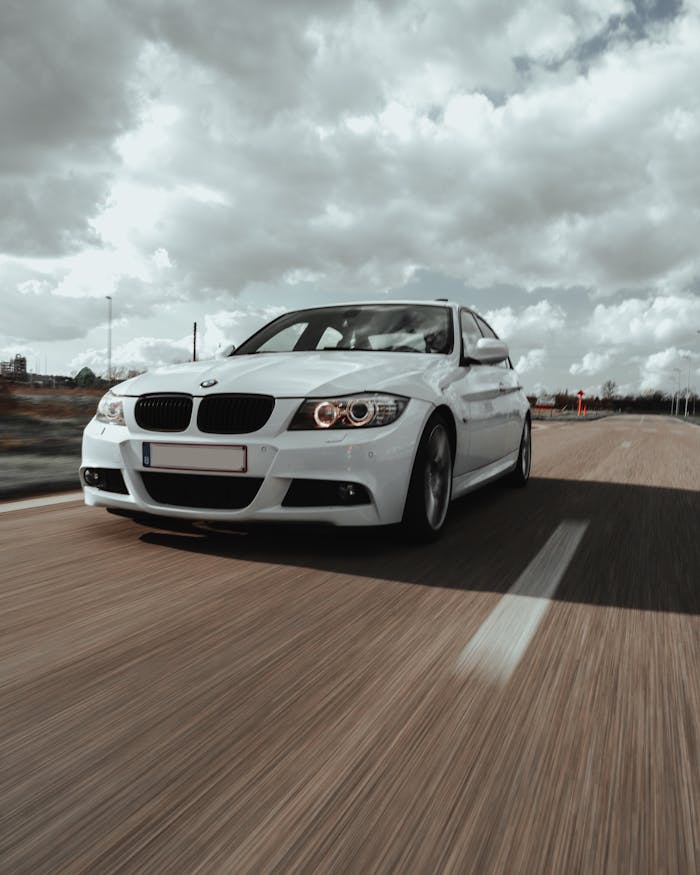 Dynamic shot of a white sedan driving on an open road under a dramatic cloudy sky.