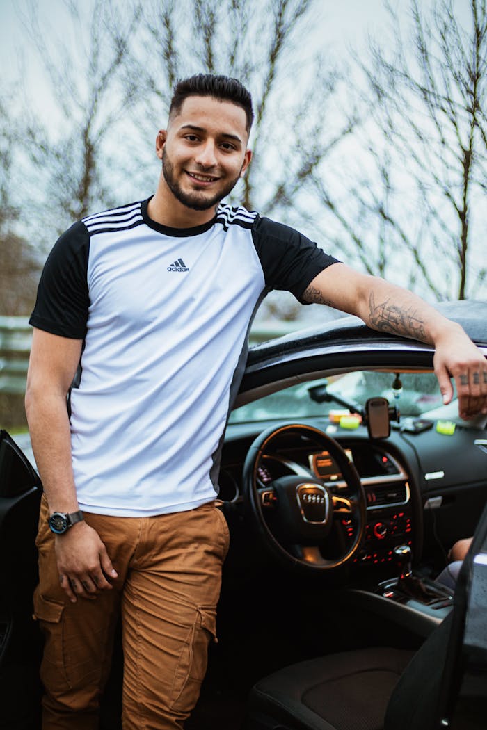 Casual man in sporty outfit smiling beside open car door, relaxed atmosphere.