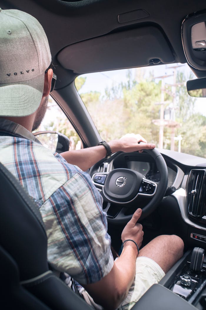 Man in casual attire driving a Volvo car, focused on steering wheel and dashboard.
