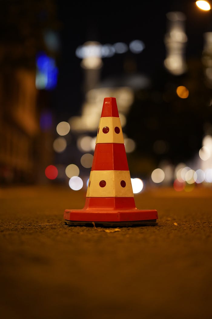 Traffic cone on an Ankara street at night with bokeh city lights in the background.