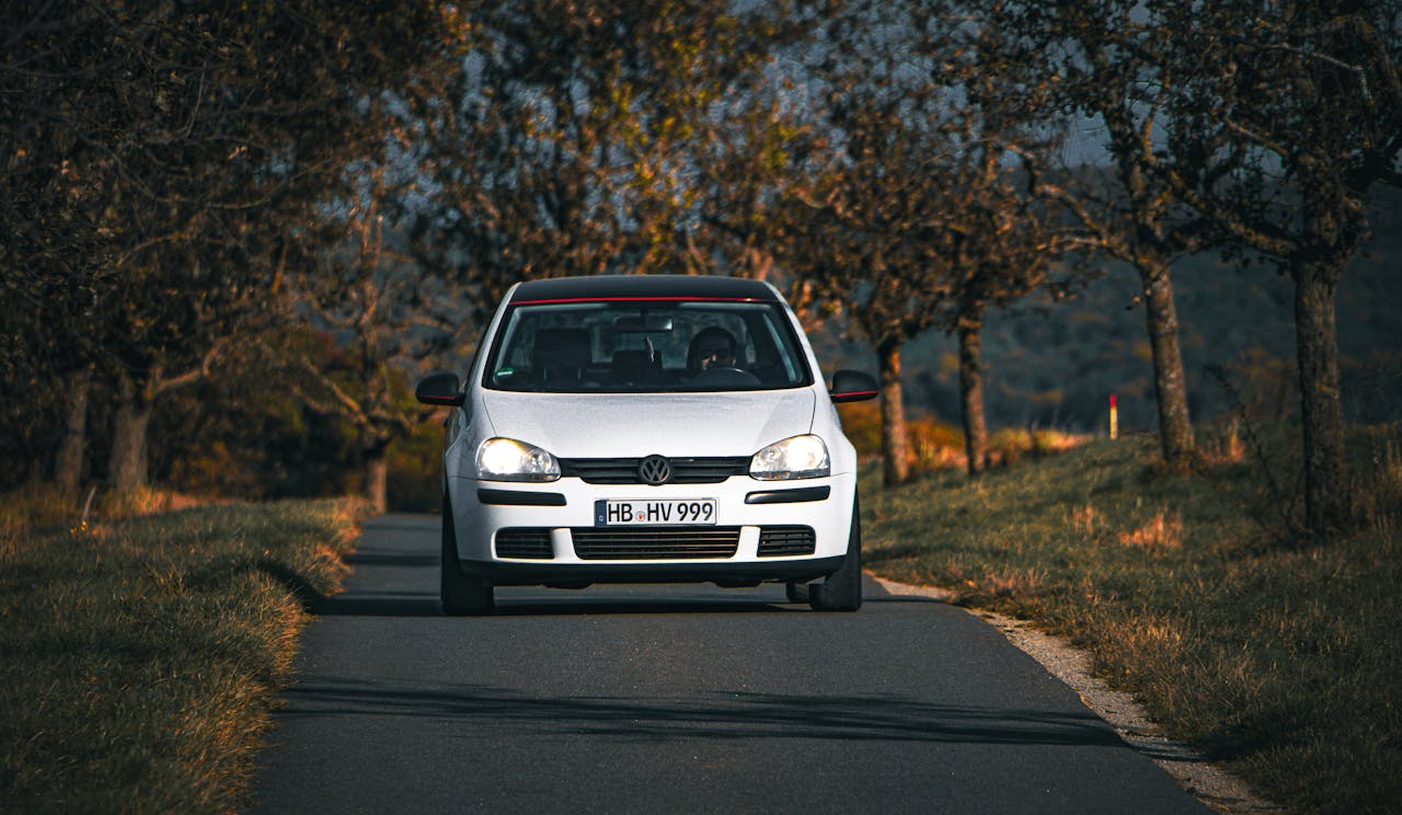 A white Volkswagen driving along an autumnal country road near Bad Mergentheim, Germany.